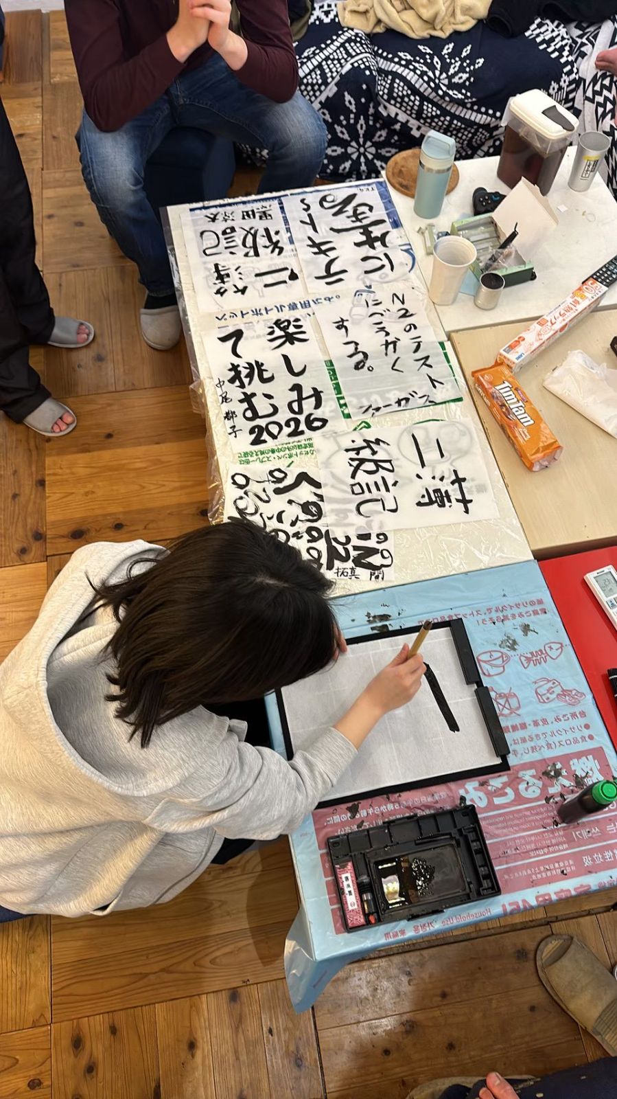 畳に半紙を広げて書き初めをするメンバー